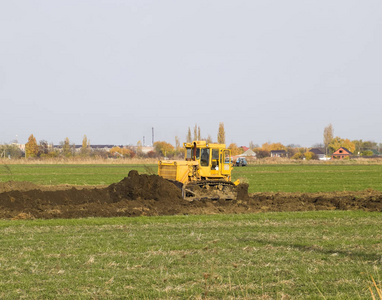 附 grederom 的黄色拖拉机使地面平整。田间排水系统的工作