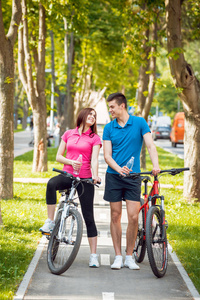年轻的白种情侣骑自行车在绿色自行车车道在晴朗的一天