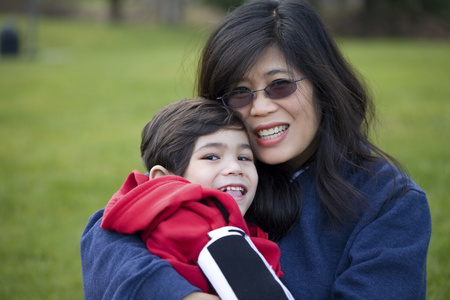 美丽的亚洲母亲抱着她残疾的儿子在公园