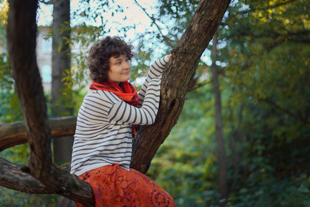 在秋天森林里坐在树上的卷曲的女孩