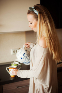 厨房里有个迷人的女人从壶里倒了一杯热茶。早上吃早饭