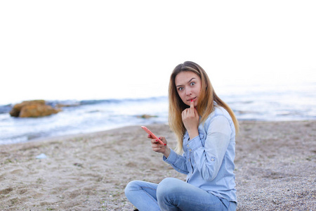 可爱的女孩带微笑电话喋喋不休的讲话 坐在海滩 n