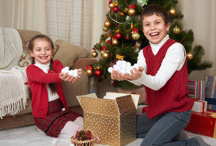 孩子打开礼品盒附近的圣诞树，显示少量的雪，在家里装修，快乐的情绪，冬天假日概念
