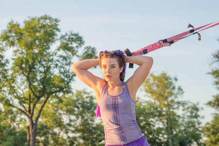 锻炼与悬浮带在室外健身房, 适合妇女训练清晨在公园, 日出背景