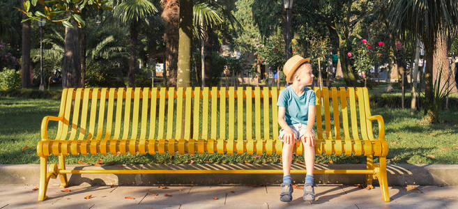 在公园的长凳上坐在帽子的孩子。横幅版