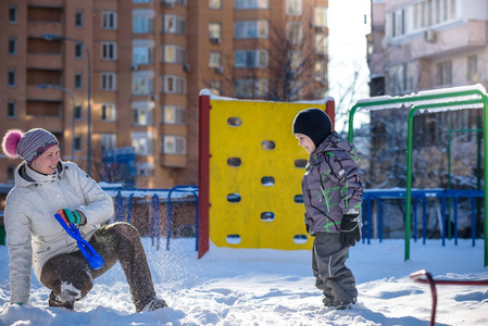 母亲和儿子享受美丽的冬天的一天在户外，玩雪在城市