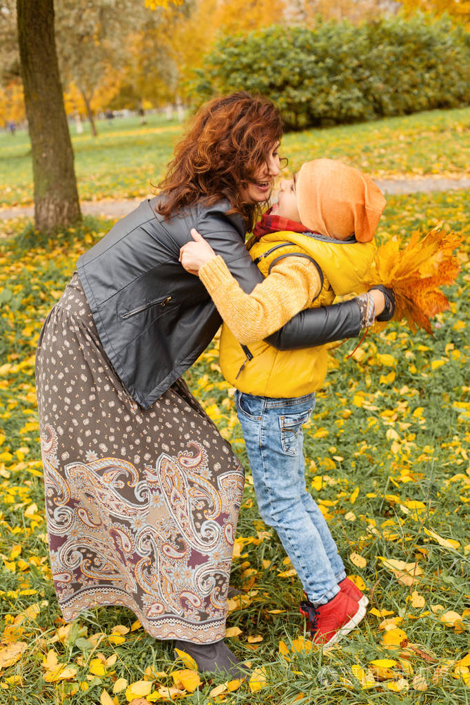 愉快的母亲和孩子男孩拥抱在秋天公园室外