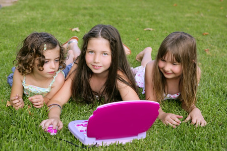 三个小女孩在草地上玩玩具电脑