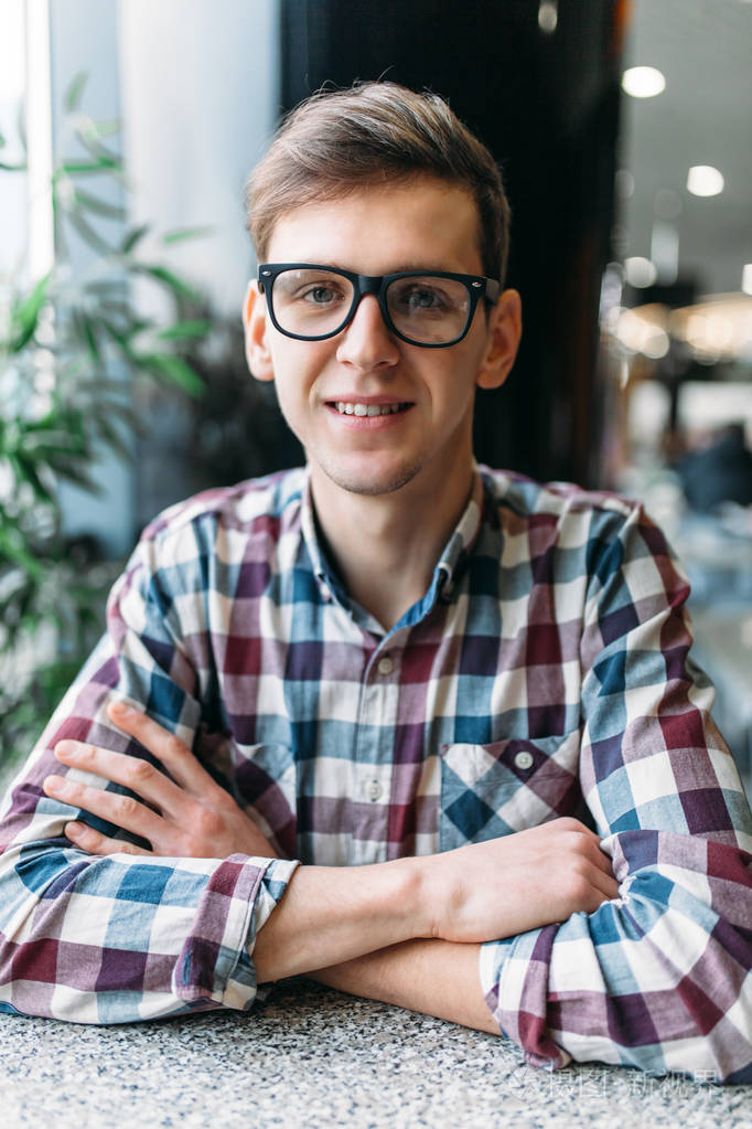 一个戴眼镜的年轻人的肖像和一个积极的心情和广泛的笑容的衬衫