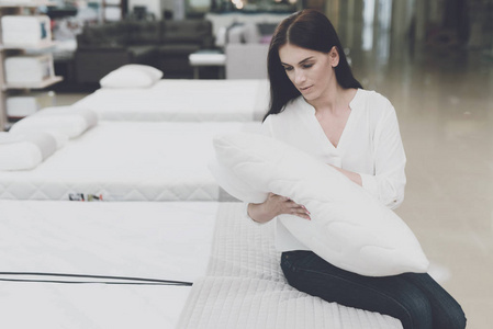 一个女人在一家大商店里挑一个枕头。她坐在床上检查她。她手里拿着它