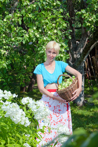 那个年轻迷人的女人在花园里拿着一篮子苹果。