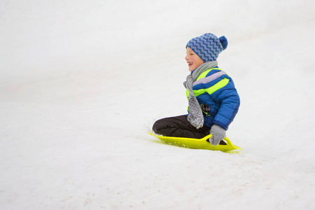 小男孩滑下山坡上的一个盘子上驾驶雪