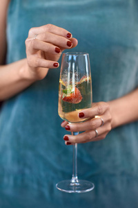 妇女滴草莓入香槟玻璃