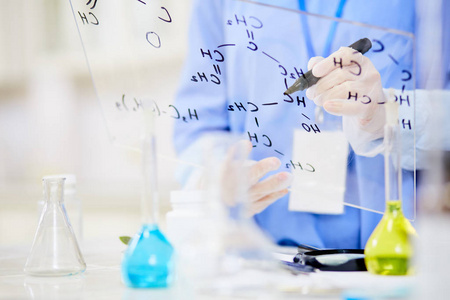无法辨认的化学家在玻璃板上写下结构公式, 同时专注于现代实验室的工作, 背景模糊