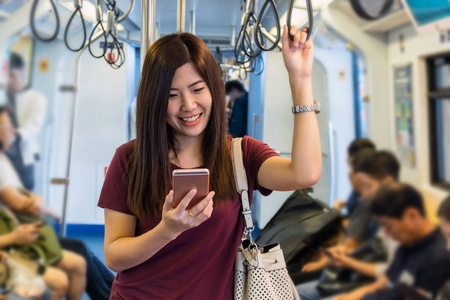 亚洲女乘客与休闲西装使用智能手机在轻轨轨道或地铁在大城市旅行