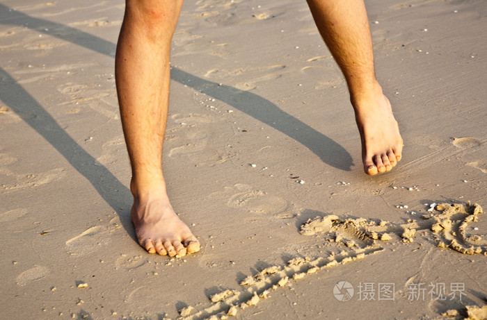 一个男孩的脚在美丽的细沙中画人物