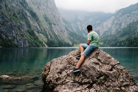 年轻的成年男子坐在岩石上看着美丽和薄雾 l