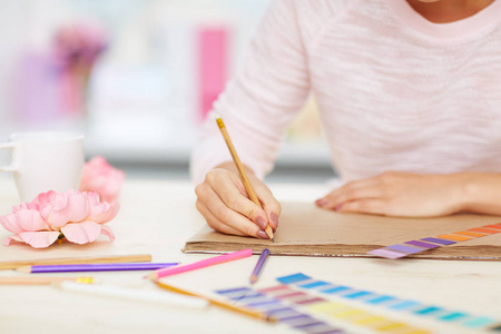 近距离拍摄的女性手中的笔记, 颜色色板, 铅笔和鲜花躺在白色的办公桌上