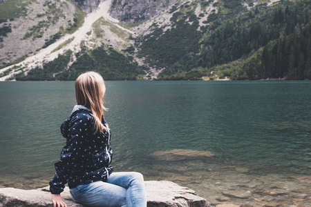 一个年轻的金发女郎坐在春湖岸边照片