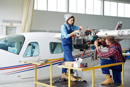 飞机维修飞机机库 两个年轻的技工, 男人和女人, 固定喷气机涡轮