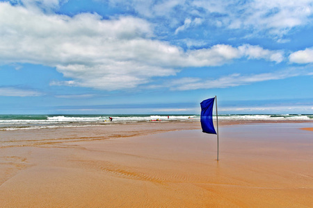 宽阔的沙滩海滩上的蓝旗宽阔的沙滩, 海浪在海面上, 蓝天白云密布.