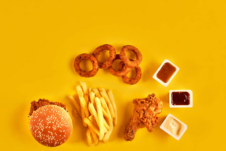 快餐菜顶视图。法式炸薯条，汉堡，沙拉酱和番茄酱的酱汁，在黄色背景上