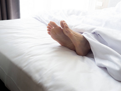 feet 的一名年轻女子躺在床上熟睡中的女人脚靠拢照片