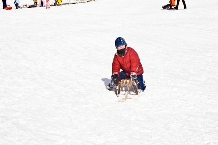 小男孩在雪白的冬天滑下山坡