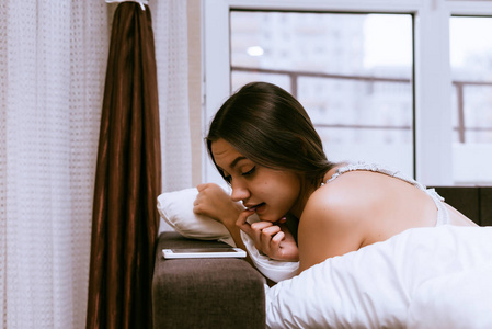 一个年轻的昏昏欲睡的女孩在毯子最近醒来, 看着她的智能手机照片