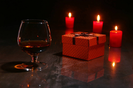 圣诞节装饰。一杯干邑或威士忌, 圣诞蜡烛和木制背景的礼品盒