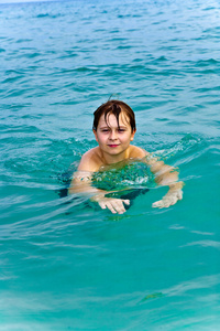 小男孩正在温暖清澈的大海里游泳，享受着假期