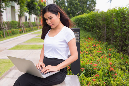 在花园长凳上使用电脑笔记本的年轻妇女