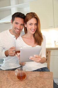 年轻夫妇在家庭厨房里用电子平板电脑