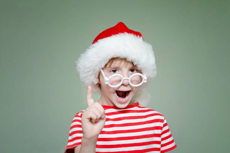 戴着眼镜的男孩和圣诞老人的帽子威胁用他的手指。肖像
