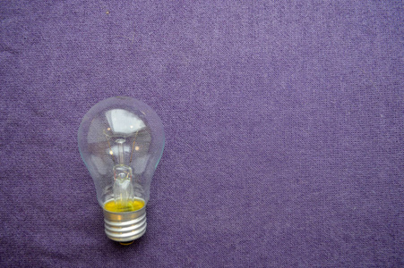 一个圆形的, 普通的, 非的白炽灯泡, 透明 socle 的紫色布背景