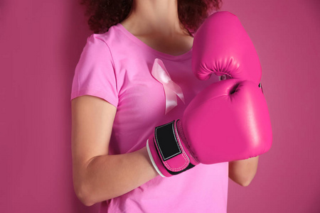 在粉红色的 t 恤和拳击手套上颜色背景的年轻女人。乳房癌认识概念