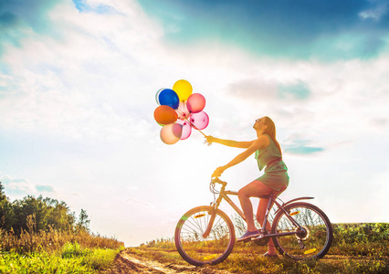 飞行周期年轻女孩在性感的礼服骑自行车飞行空气气球照片