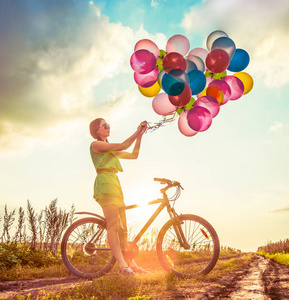 年轻女孩在的礼服骑自行车飞行空气气球