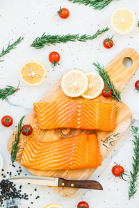 木制砧板上的生鲜鲑鱼肉柳配柠檬西红柿和其他成分健康食品风格