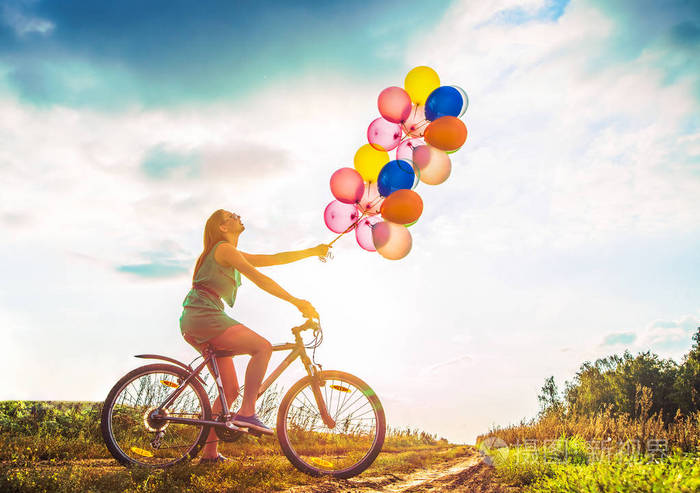 年轻女孩在性感的礼服骑自行车飞行空气气球