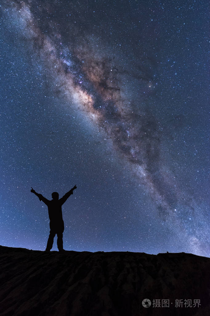 银河景观快乐的人站在山与夜晚的天空和明亮的星星在背景上的剪影