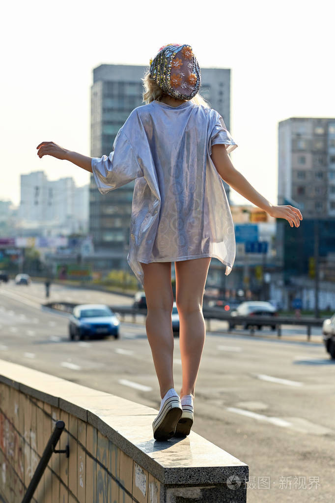 年轻的金发女孩在闪闪发光的帽子走在大街上