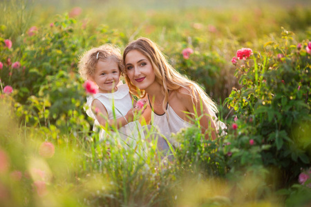 美丽的夫妇孩子女孩与漂亮的年轻母亲是走在春天花园与粉红色的花朵玫瑰花