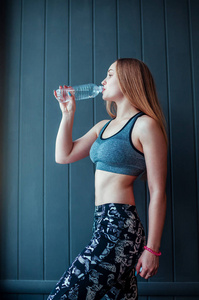 在健身房喝水的年轻女子的照片。在窗前休息和喝水的肌肉女性