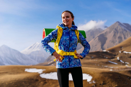 穿着蓝色夹克的年轻快乐女孩带着背包和帐篷沿高加索山脊旅行