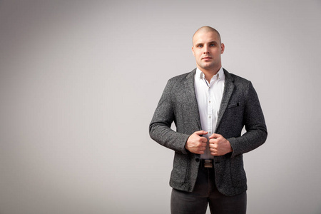 一个穿着白色衬衣的光头男子, 灰色西装自信地看着相机, 双手在他的