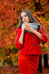 漂亮的女孩在一个秋天的背景上喝咖啡