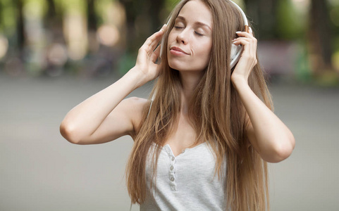 漂亮的女孩与她在街上的耳机听音乐