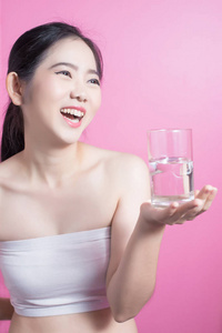 健康的亚洲年轻美丽的妇女饮用水, 秀丽面孔自然化妆, 隔绝在桃红色背景