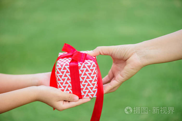 母亲递给孩子一个带红丝带的礼品盒.假日,礼物,圣诞节和幸福概念